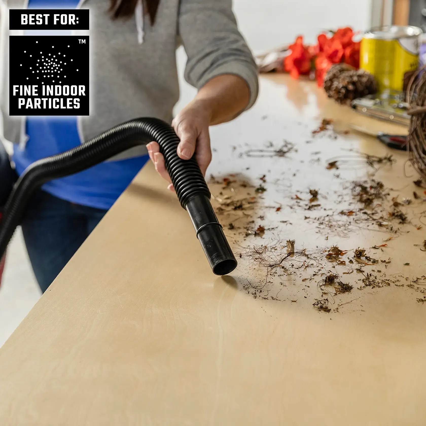 Person vacuuming fine dirt off indoor work bench with wet/dry vac hose