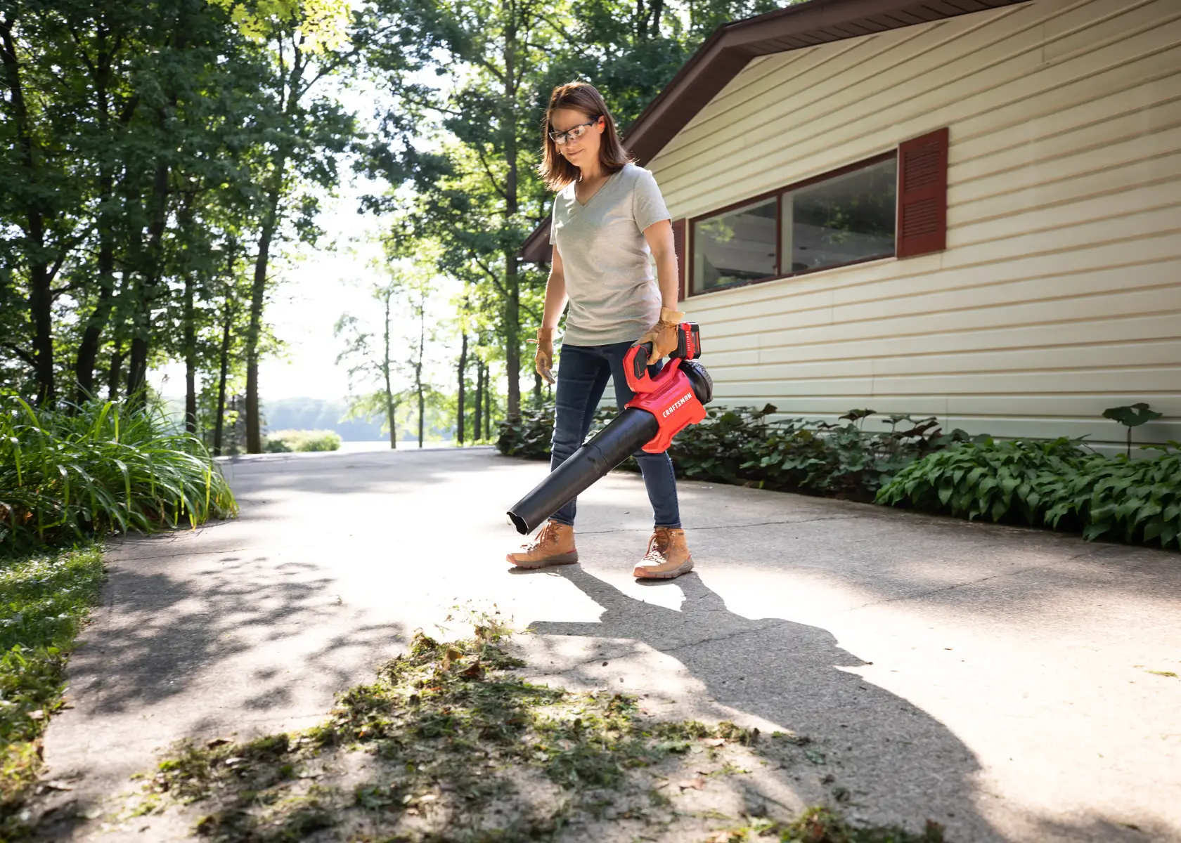 CRAFTSMAN V20 BRUSHLESSRP Blower clearing grass off driveway home in background