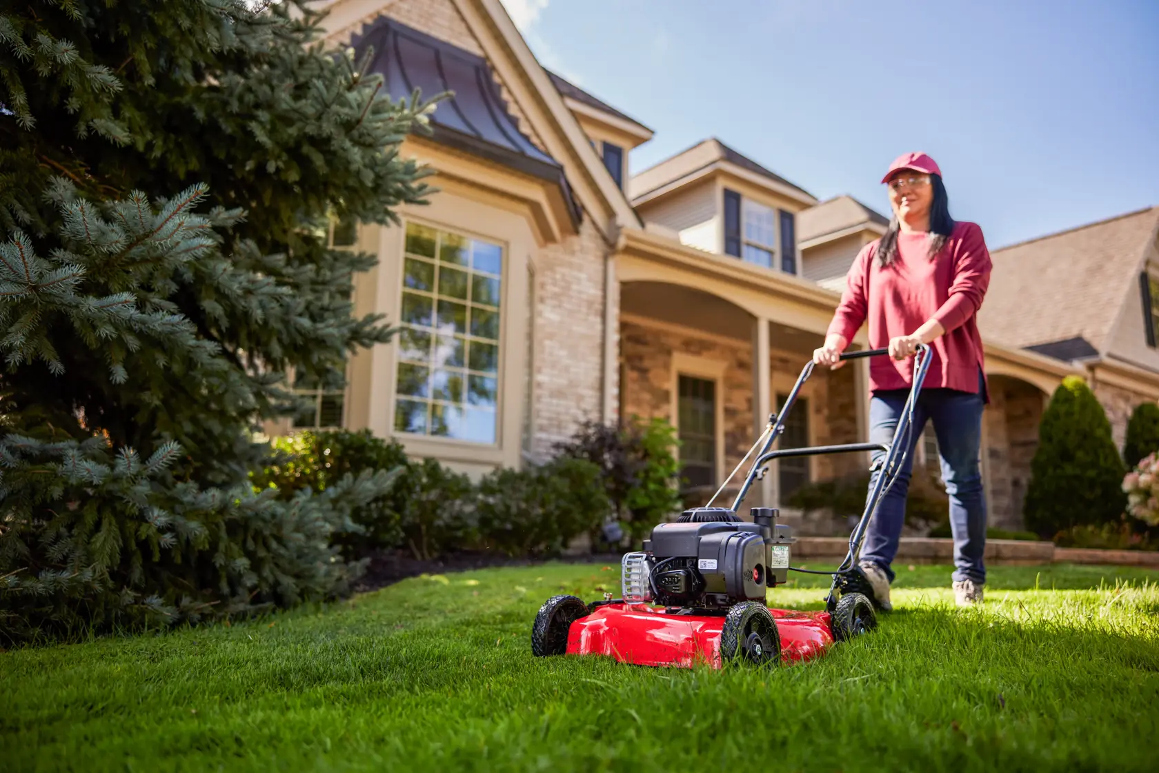 Side view looking upward from the ground of woman cutting grass with M090 Walk-behind Lawn Mower
