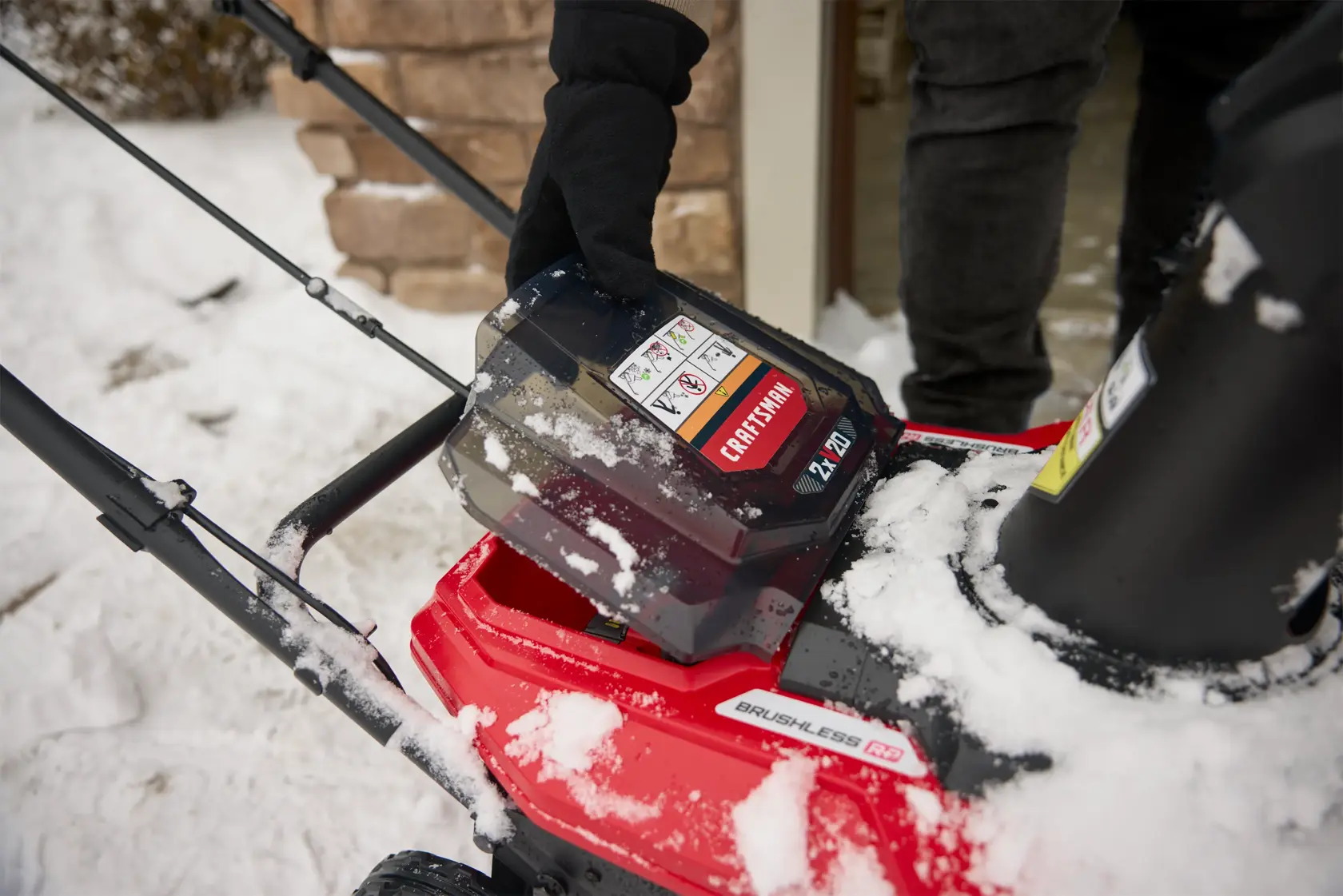 Photo of a CRAFTSMAN snow blower, SKU CM32AB2B1CB93, with a close-up of a battery being inserted, snow visible.