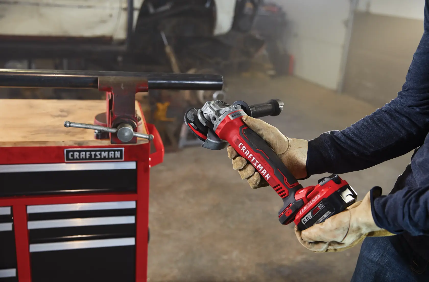 Photo of Craftsman cordless grinder CMCB2046-CK held by gloved hands in a workshop near a red tool chest.