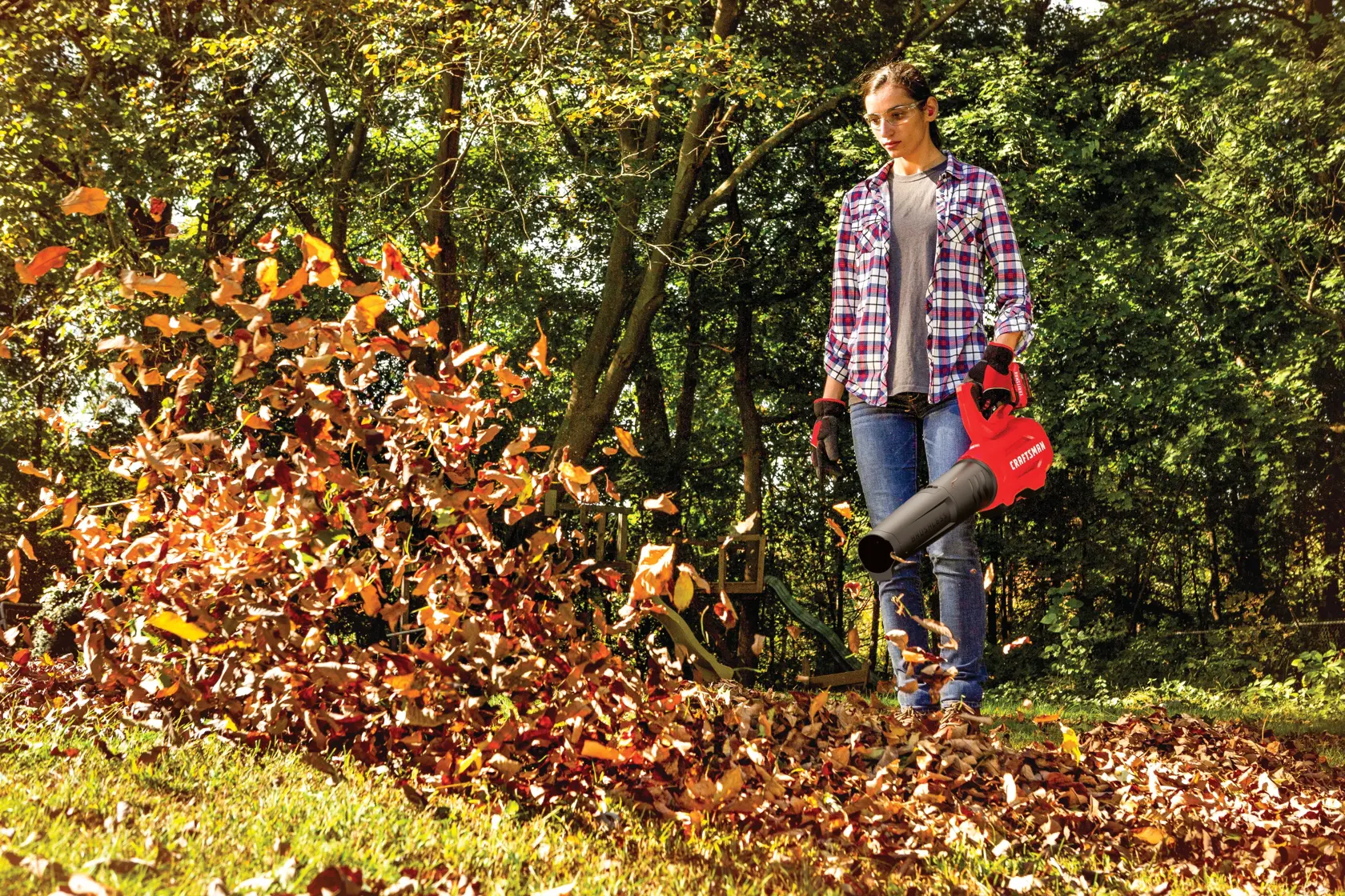 Brushless cordless axial blower being used for cleaning dead leaves from lawn by person.