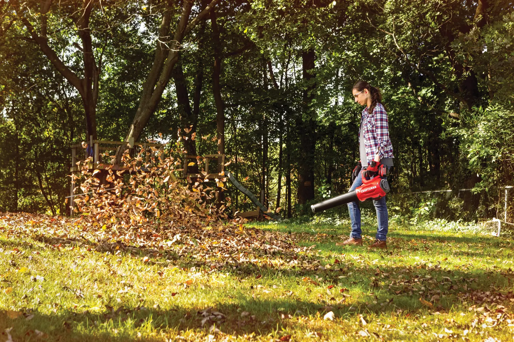 Brushless cordless axial blower being used for cleaning dead leaves from lawn by person.