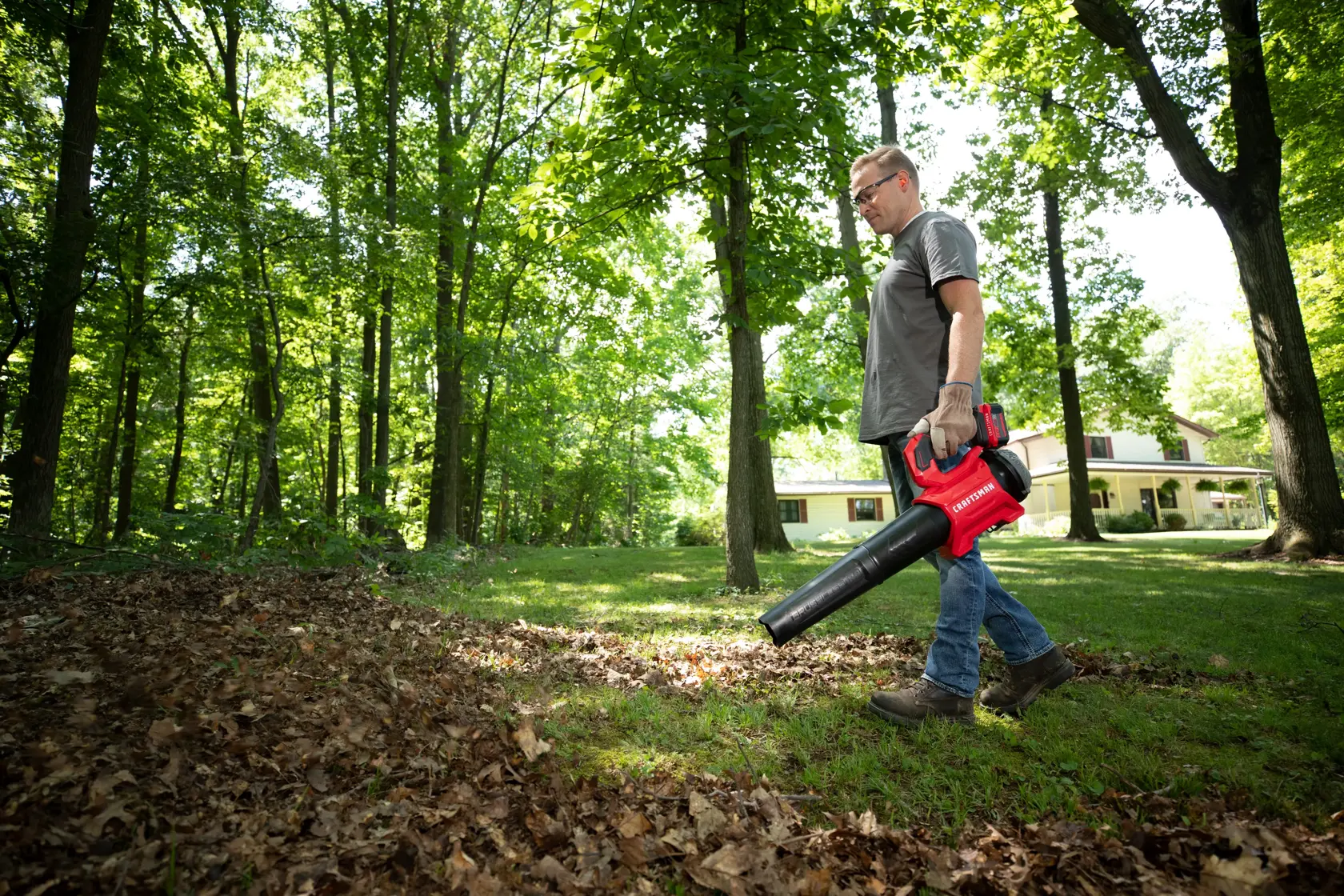 CRAFTSMAN V20 BRUSHLESSRP Blower clearing leaves off grass in a wooded area with tree coverage