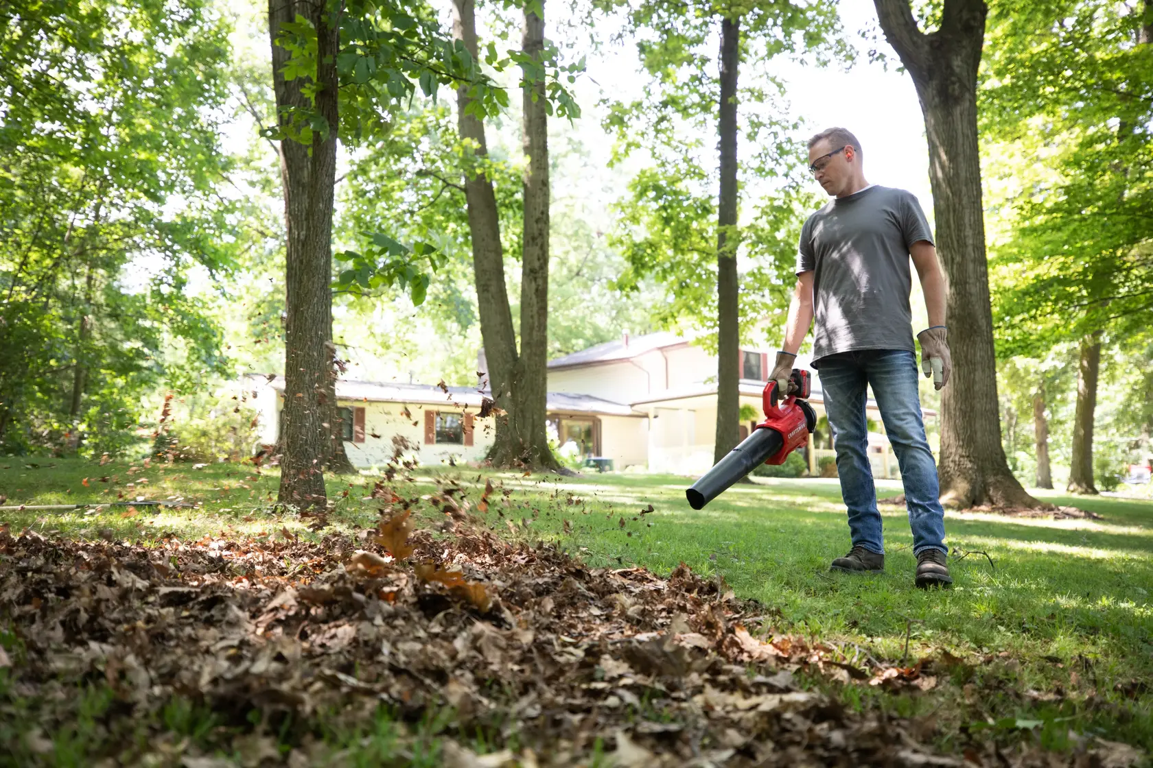 CRAFTSMAN V20 BRUSHLESSRP Blower clearing leaves off grass in a wooded area with tree coverage