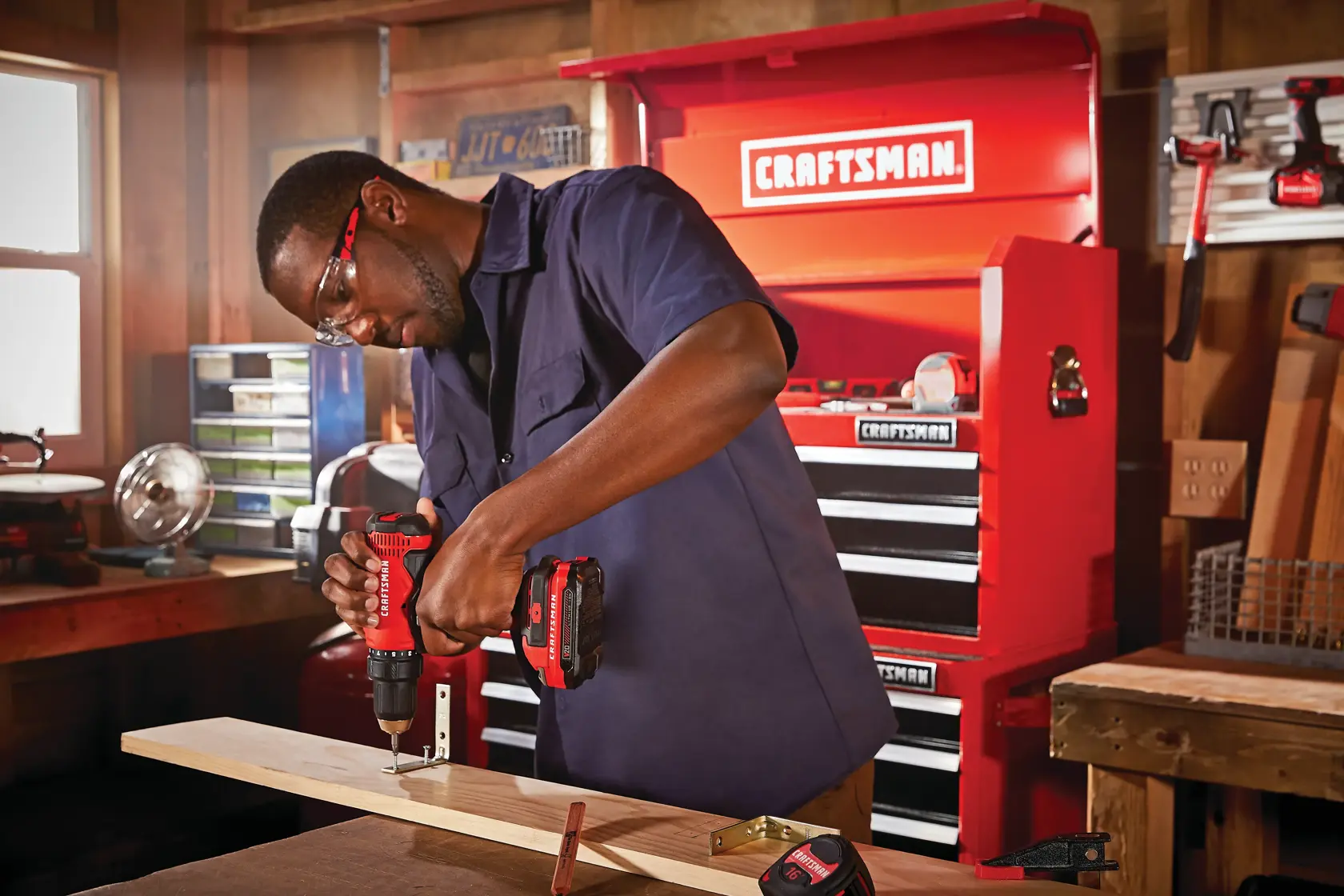 Half inch cordless drill and driver kit 2 batteries being used for fixing metal hook on wooden plank by person.
