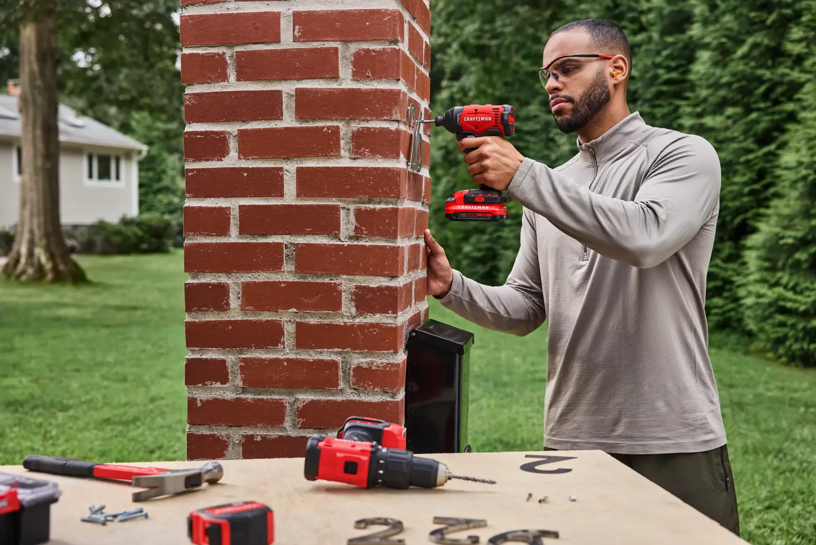 Man drilling into brick to hang house number with the CRAFTSMAN� V20* Brushed Impact Driver