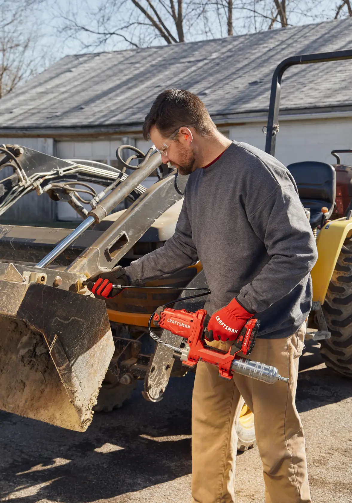 Photo of end-user applying grease with grease gun to farm equipment.