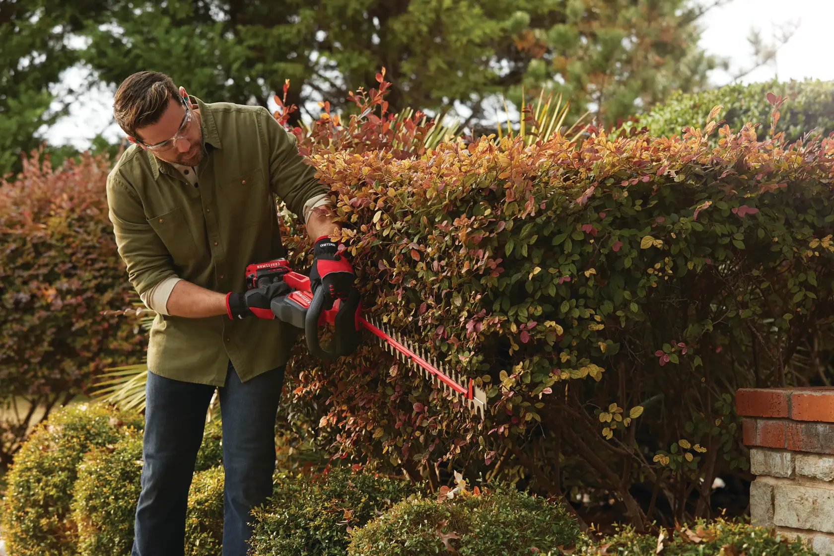 Cordless 22 inch hedge trimmer kit 2 ampere hours being used to level sides of hedge.