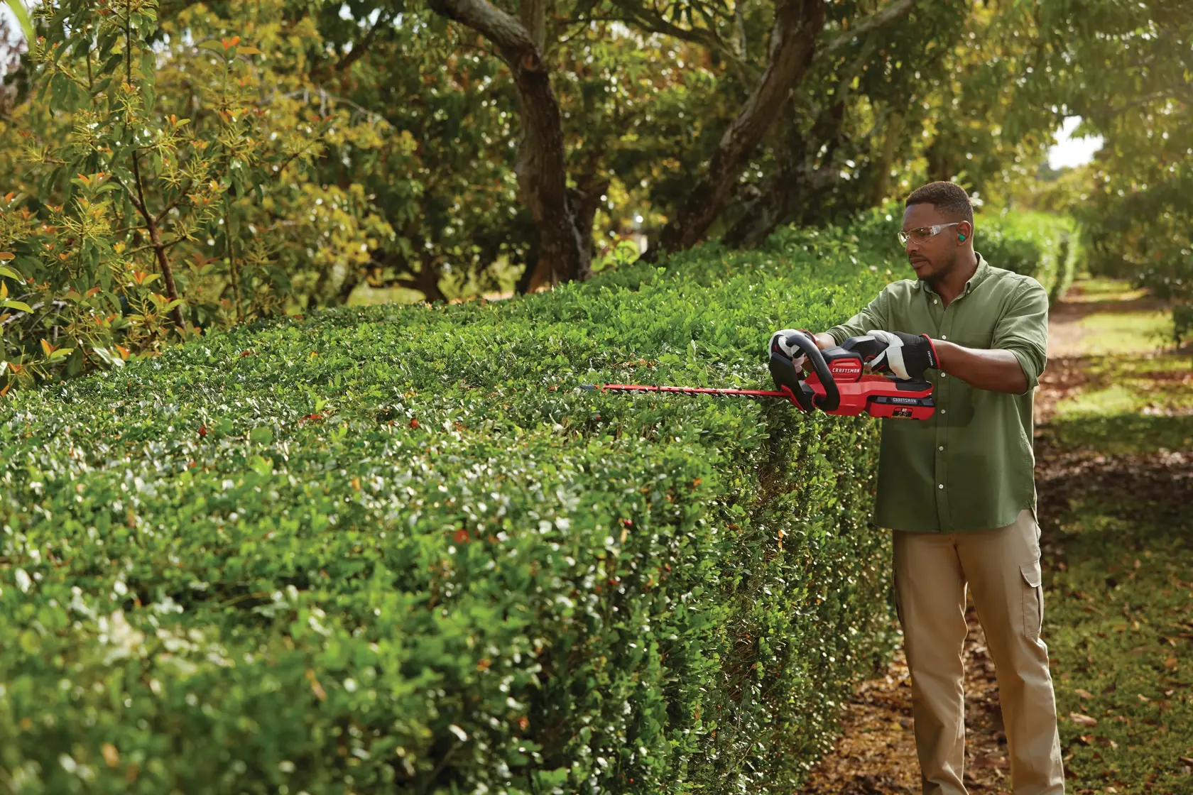Cordless 24 inch hedge trimmer kit 2.5 Ampere hours being used to level hedge top.