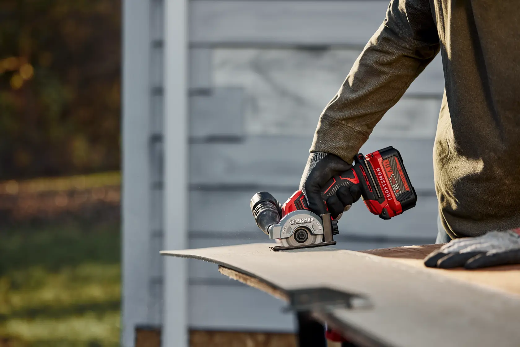 Photo of a person using a Craftsman compact saw CMCM300B to cut a sheet material outdoors.