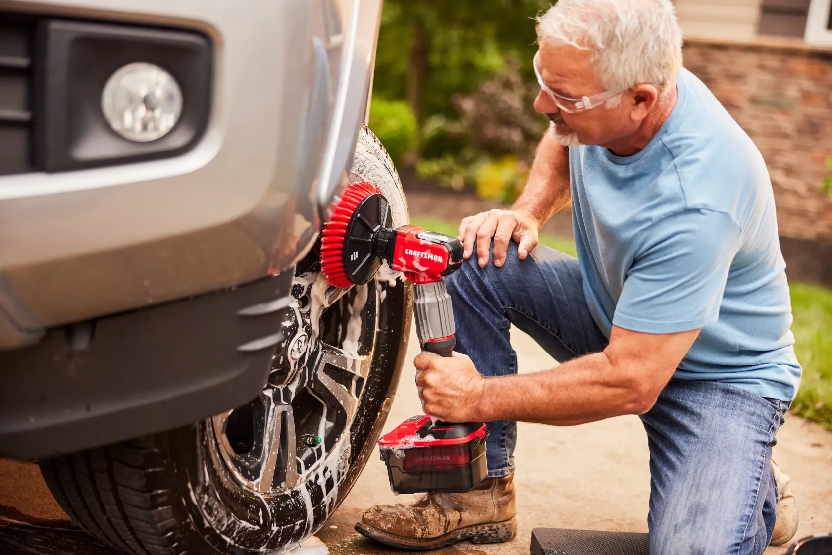 Photo of a person cleaning a car wheel with a CRAFTSMAN power scrubber, SKU CMCPS520B, outdoors.