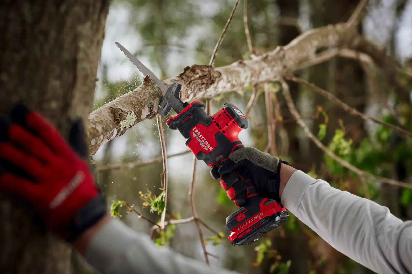 Photo of Craftsman cordless reciprocating saw SKU CMCS340B cutting a tree branch outdoors, tool held with gloves.