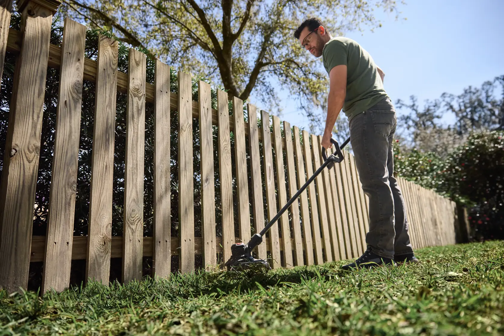 Photo of CRAFTSMAN string trimmer, SKU CMCST930P1, trimming grass along a wooden fence outdoors.