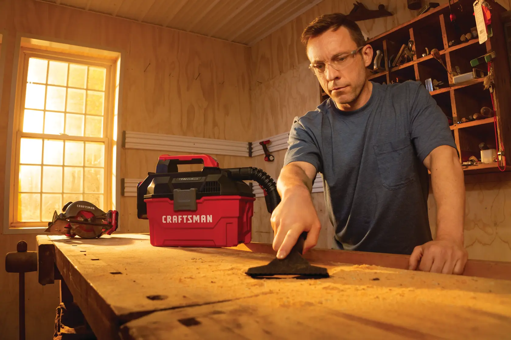 20 volt cordless 2 gallon wet dry vacuum being used by a person to clean wooden work station.
