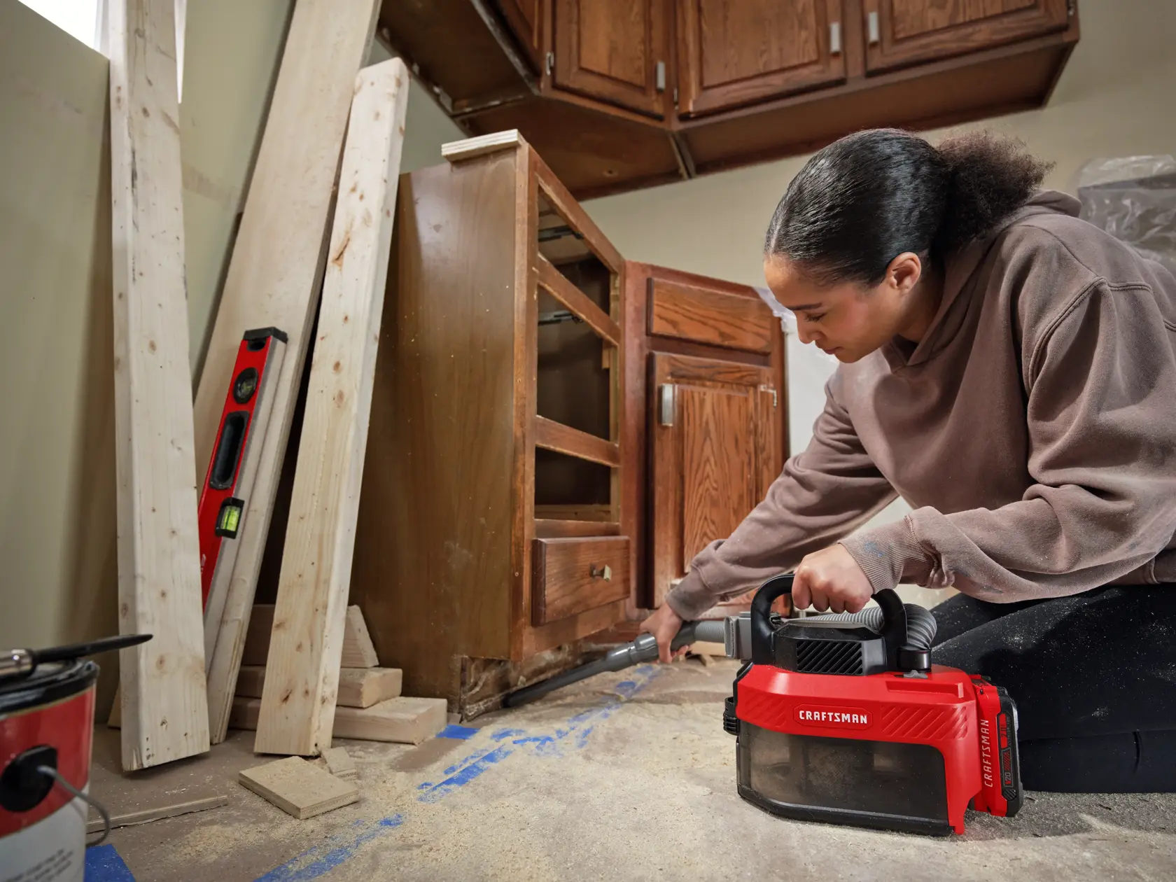 Person using a red CRAFTSMAN handheld vacuum to clean debris near wooden cabinets during a renovation project.