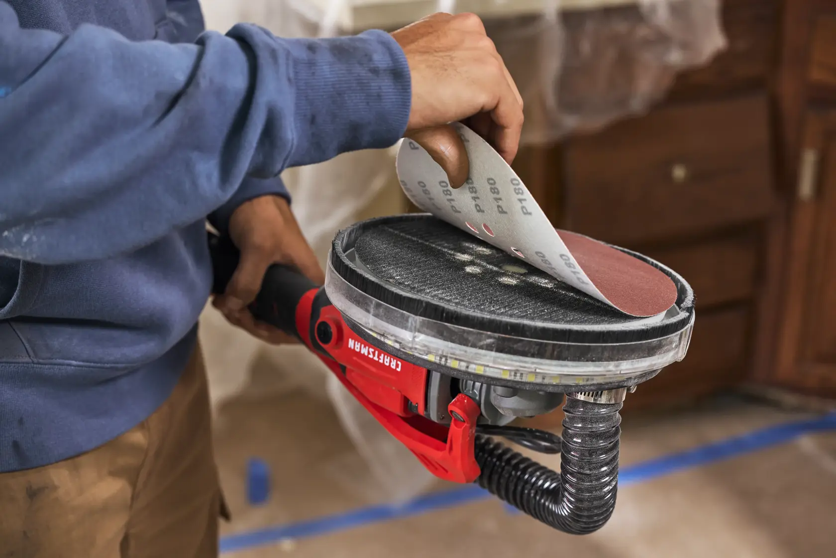 A person attaches sandpaper to a CRAFTSMAN electric sander during a home improvement project.