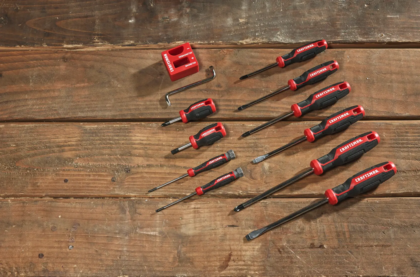 A set of nine CRAFTSMAN screwdrivers, an Allen wrench, and a red holder, displayed on a wooden surface. The screwdrivers vary in size and type, featuring red and black handles.