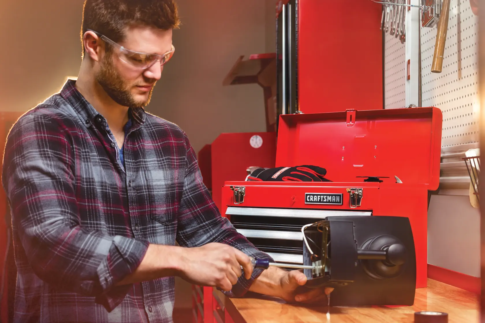 Portable 20 and 5 tenths inch Ball bearing 3 Drawer Red Steel Lockable Tool Box containing tools in use by person working on inner mechanism of a device.
