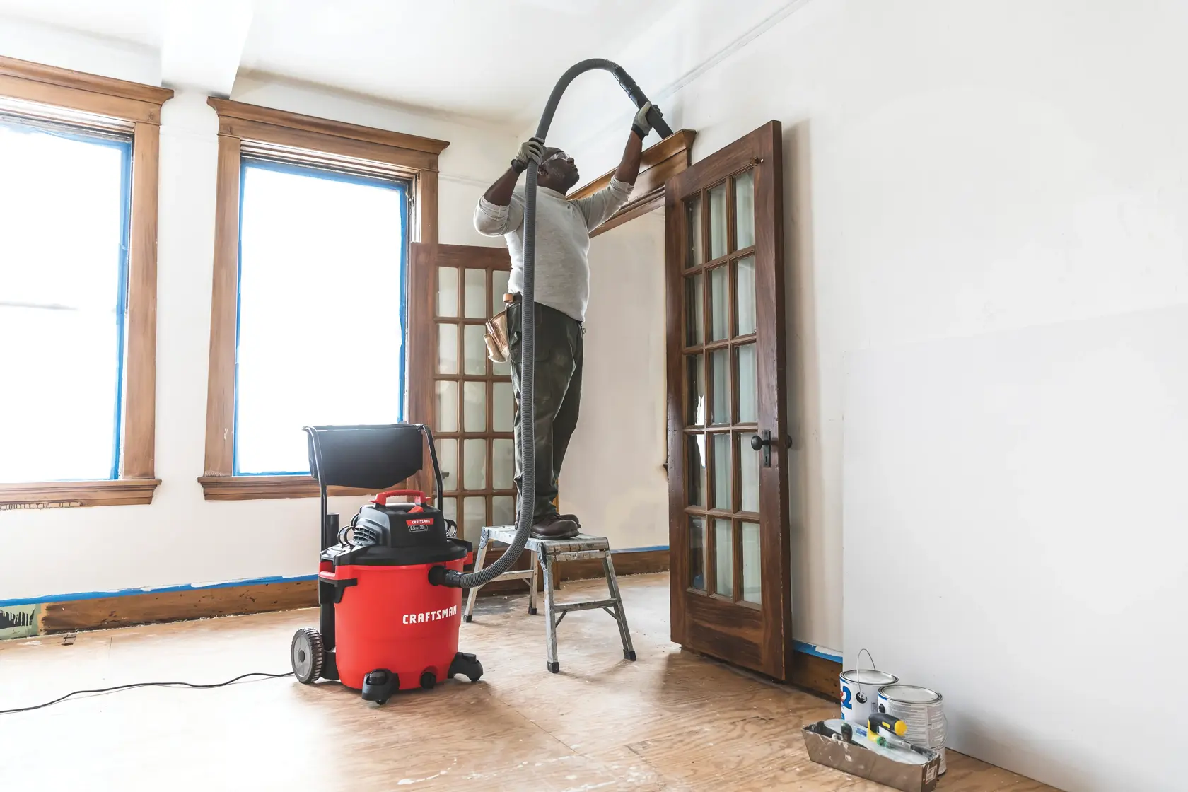 20 gallon 6.5 H P wet dry vacuum with cart being used by a person to clean wooden door frame.