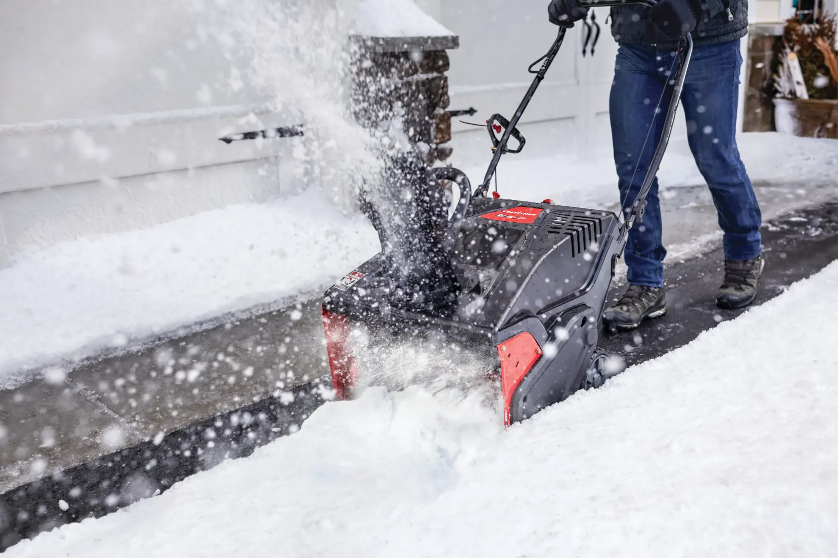 CRAFTSMAN Electric Start Single-Stage Snow Blower in front view blowing snow in driveway with jeans and boots