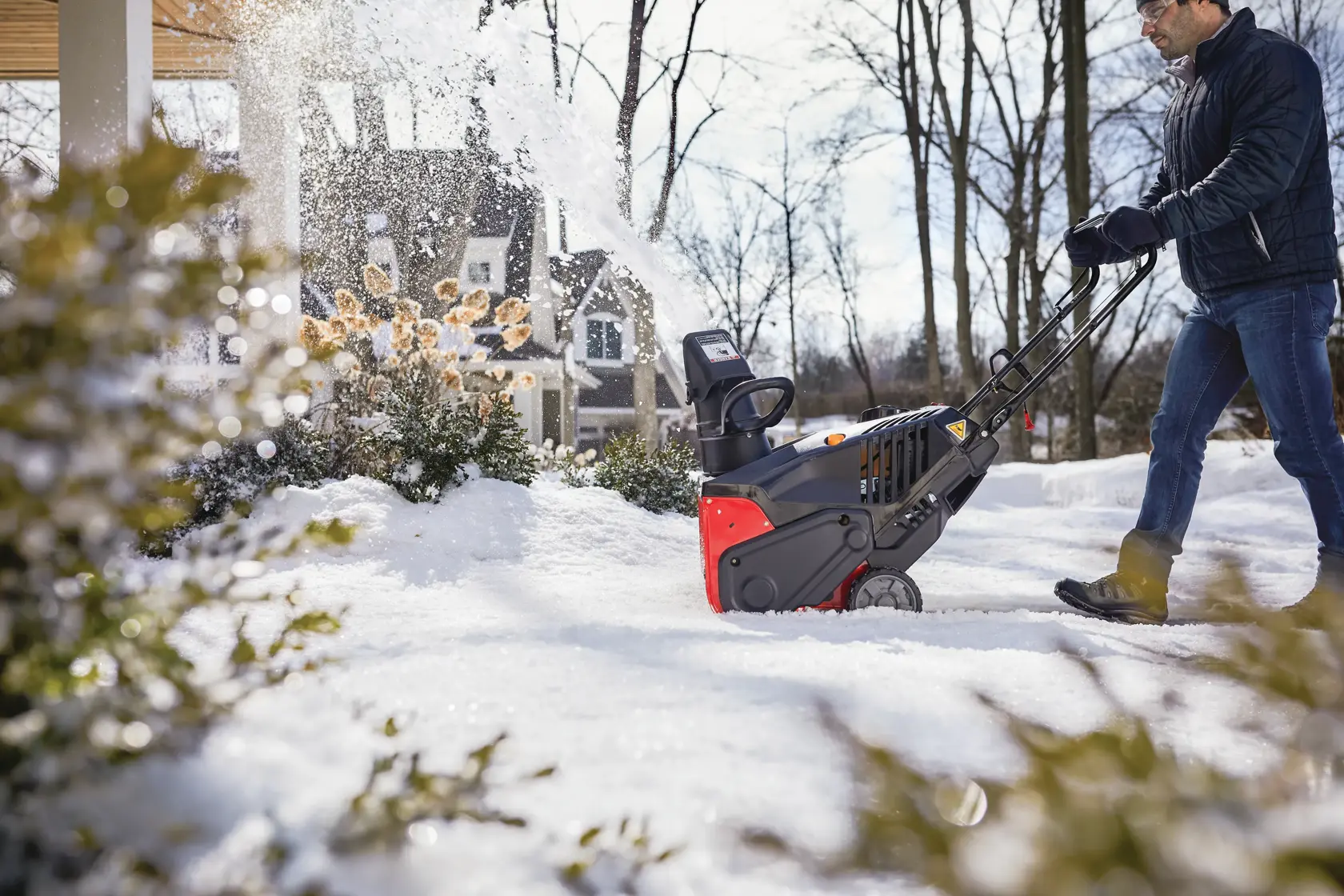 CRAFTSMAN Electric Start Single Stage Snow Blower in side view blowing the snow off the house’s walkway in black coat 