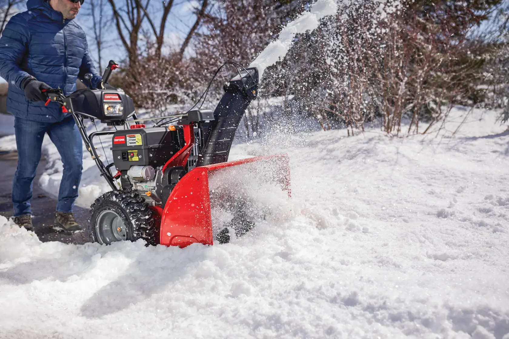 CRAFTSMAN Electric Start 3-Stage Snow Blower blowing the snow off a sidewalk in a yard in side view in blue jacket