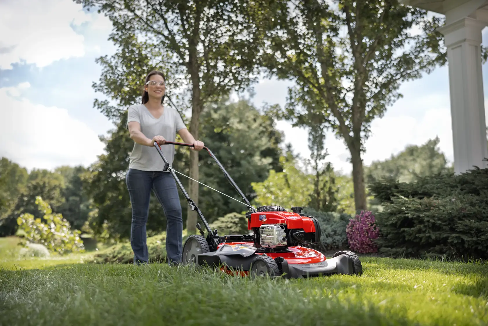 CRAFTSMAN 140cc Push Mower in side view mowing the backyard lawn with maroon shirt