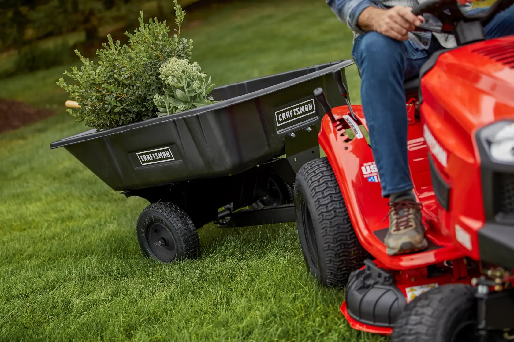 CRAFTSMAN T100 36 In. 11.5 Hp* Gear Drive Riding Mower pulling attachable wheelbarrow with plants