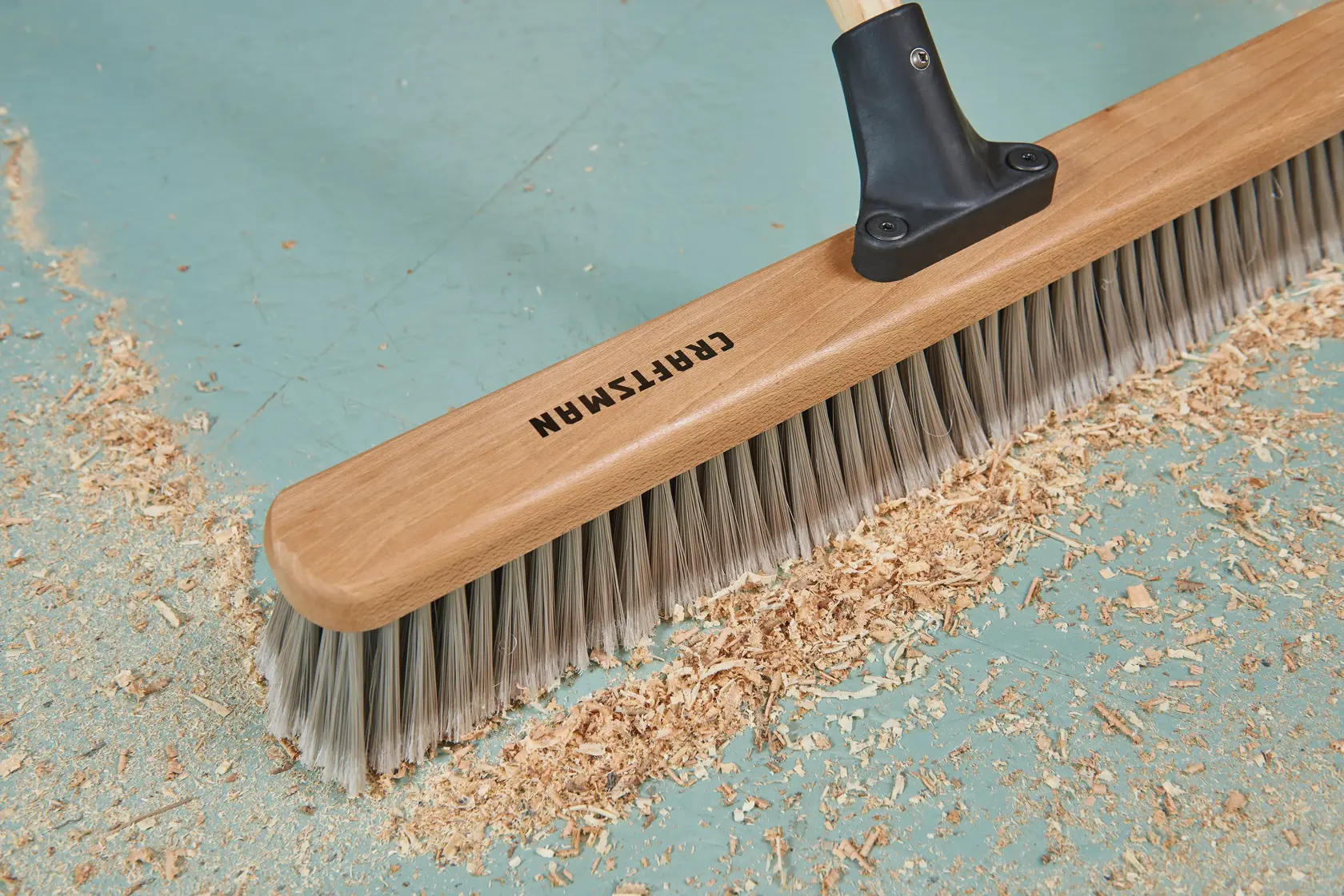 24 inch shop-and-garage push broom head close up cleaning sawdust on vinyl floor