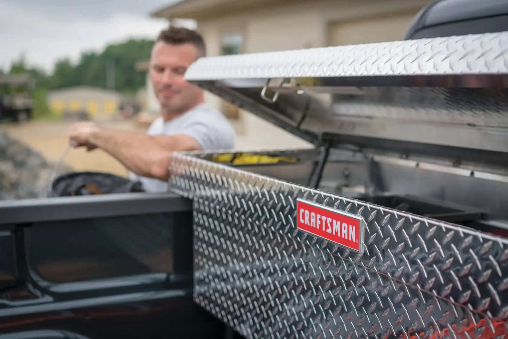 Photo of CRAFTSMAN CMXTBAK1000901 truck bed tool box with diamond plate pattern, lid open in pickup truck bed.