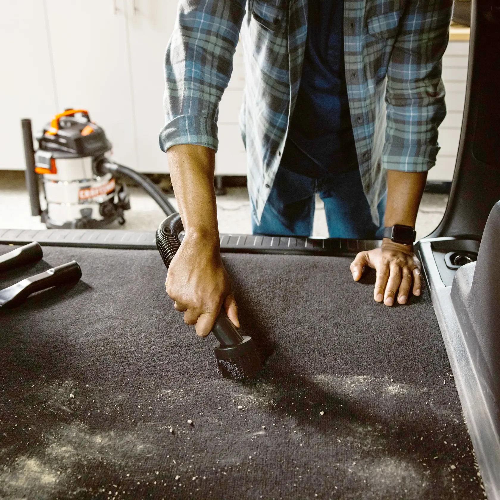 Photo of person using CRAFTSMAN wet/dry vacuum CMXZVBE38662 to clean a car trunk's carpet with debris visible.