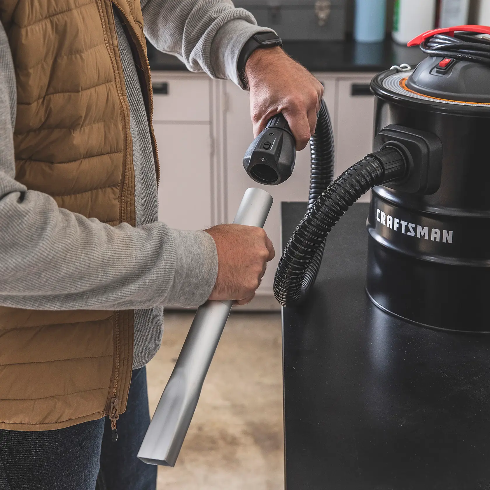 Homeowner standing by counter installing metal accessory onto hose of CRAFTSMAN 5 Gallon Ash Vacuum