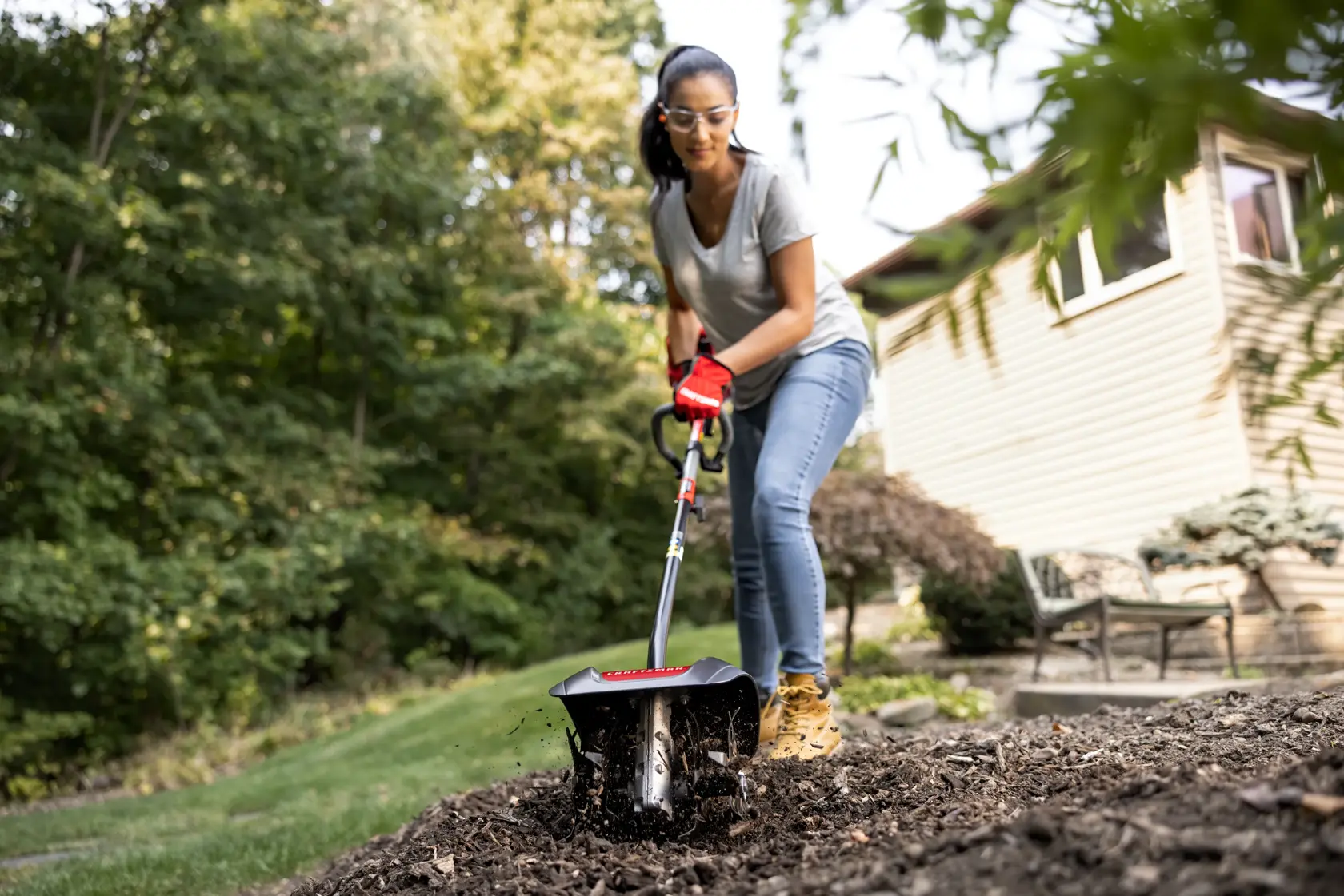CRAFTSMAN cultivator attachment head in front view tending to mulch in backyard in gray shirt and jeans