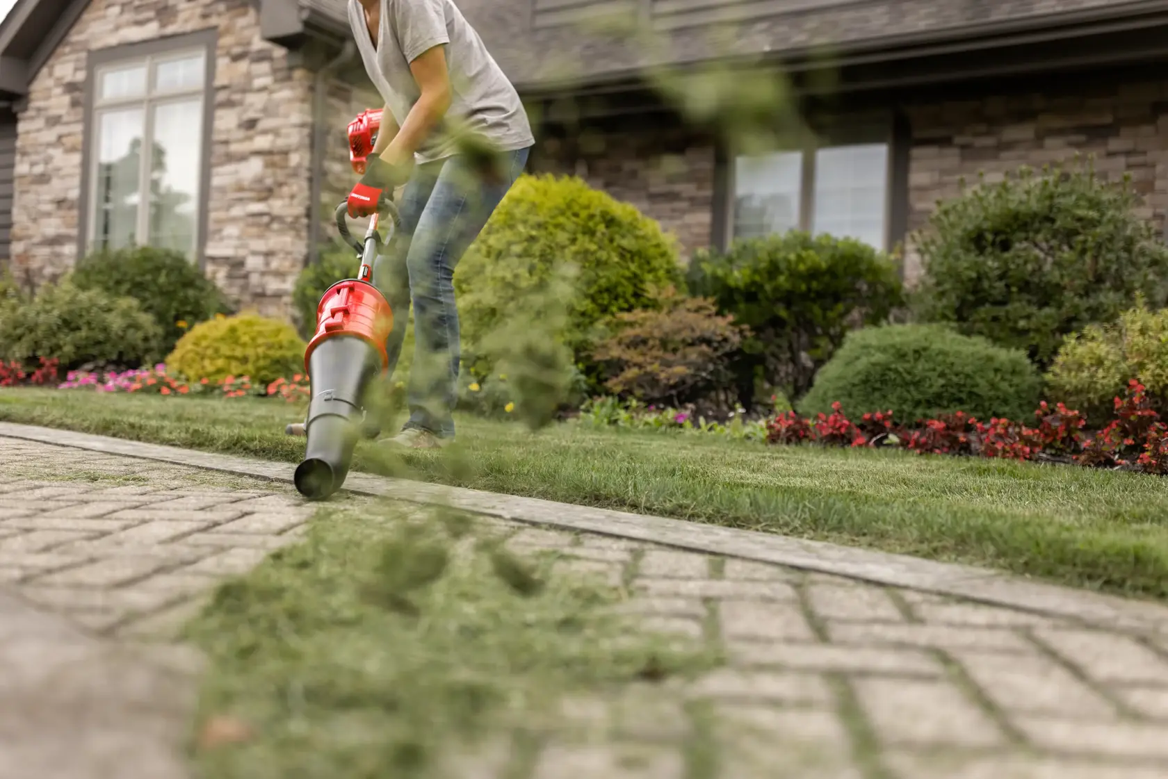 CRAFTSMAN cone blower attachment head blowing grass off sidewalk in front of a house in gray shirt and jeans