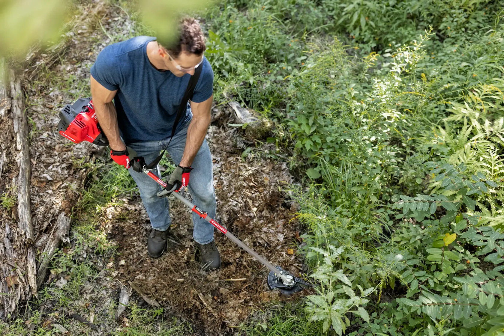 CRAFTSMAN brushcutter attachment head from top view trimming brush in the woods in blue shirt and jeans